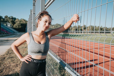 Portrait of smiling young woman standing by fence