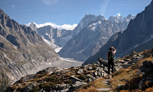 Woman standing on rock by mountains against sky