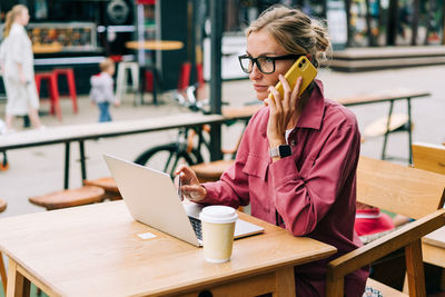 Young attractive business woman in glasses sitting at a table in a cafe working on a laptop.