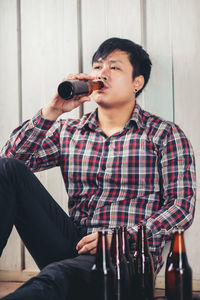 Young man drinking beer in bottle while sitting on table