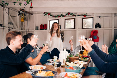 Happy male and female friends raising wineglasses in cottage