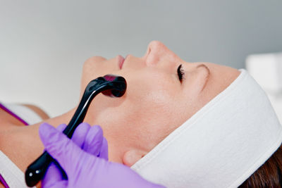 Close-up of woman lying down with while beautician using cosmetic roller on face at spa