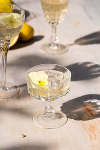 High angle of glass goblet of cocktail garnished with white flower and placed on table during party on sunny weekend day