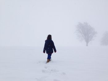 Rear view of woman walking on snow covered field