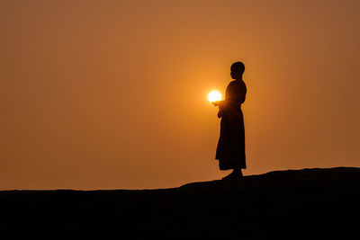 Silhouette woman standing against orange sky