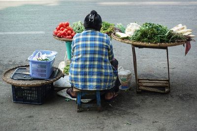 Woman selling vegetables and orher herbs on the streets. urban everyday life scenery. rear view.