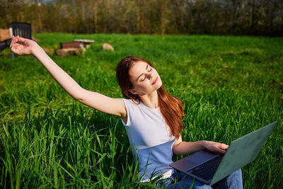 Young woman using mobile phone while sitting on grassy field
