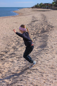 Beautiful little blond hair girl with long braid jumping on sea beach. smiling child walking on sand