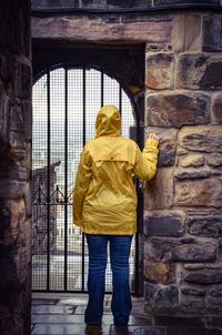 Rear view of woman in yellow raincoat standing against door of building