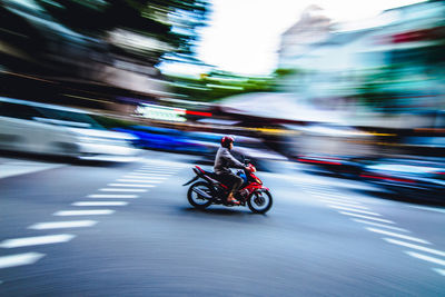 Person riding bike on road with blurred motion of city in background