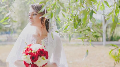 Bride looking away while standing by tree