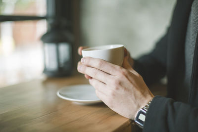 Midsection of man holding coffee cup on table