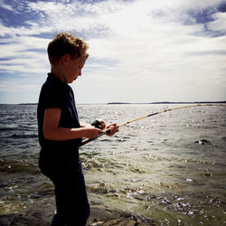 Side view of boy standing on beach against sky