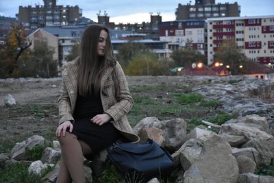 Woman sitting on rock at field in city