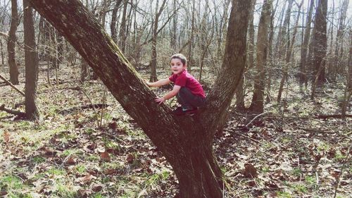 Portrait of young woman standing on tree trunk in forest