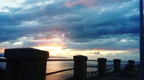 Silhouette railing by sea against sky during sunset