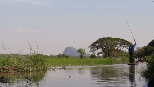 Man fishing by lake against sky