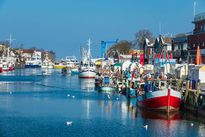 Boats moored at harbor against clear blue sky