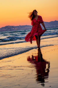 Woman with arms raised on beach against sky during sunset