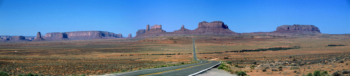 Road passing through landscape against clear blue sky