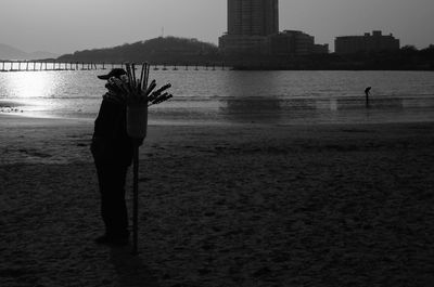 Silhouette man standing on beach against sky in city