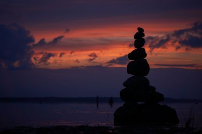 Stack of pebbles on beach against sky during sunset