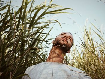 Low angle view of young man looking away while standing amidst plants