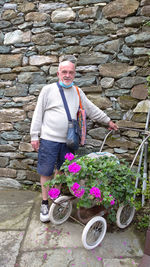 Portrait of man holding flower while standing against brick wall