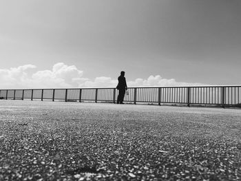 Man standing on railing against sky