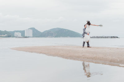 Newlywed couple standing on beach against sky