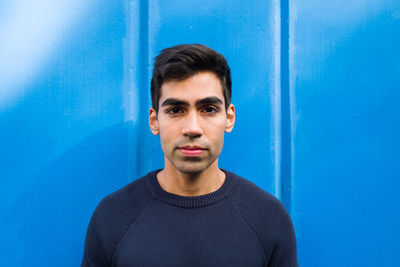 Portrait of the young man looking at the camera standing against blue background