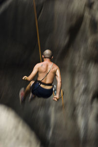 Low angle view of shirtless man rappelling on rock formation