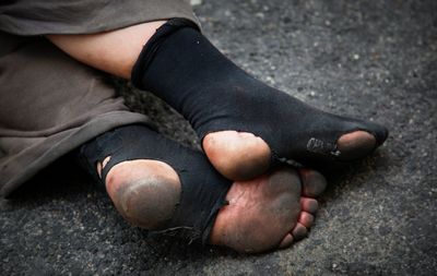 Low section of beggar wearing torn socks