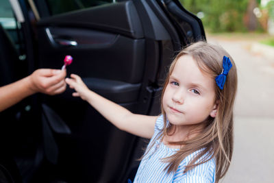 Portrait of cute girl taking chocolate from person in car