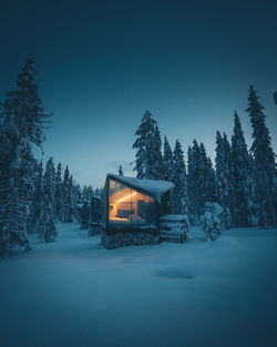 Snow covered cabin and trees against clear sky