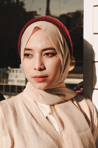 Young woman in hijab looking away against wall