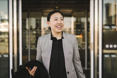 Happy businesswoman holding coat walking out door