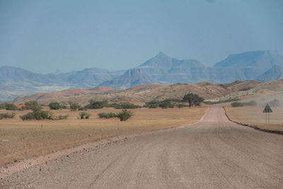 Desert gravel road in a dry yet colourful and hilly landscape of etosha mountains in background