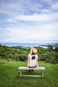 Rear view of woman sitting on field against sky