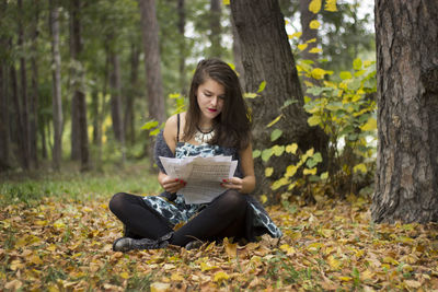 Young woman sitting on book in forest