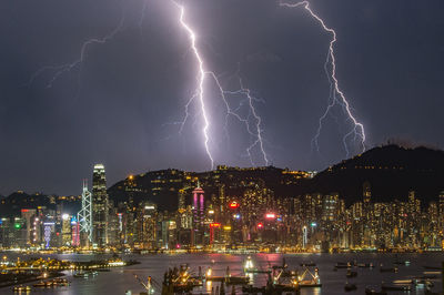 Illuminated city at victoria harbour against lightning at night