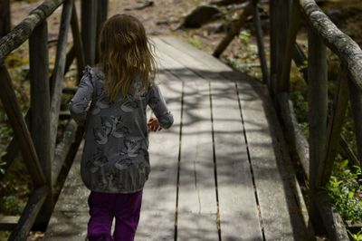 Rear view of girl walking on footbridge in forest