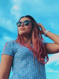 Low angle view of woman with hand in hair standing against sky