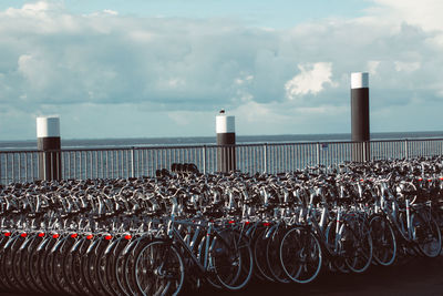 Bicycles on railing by sea against sky