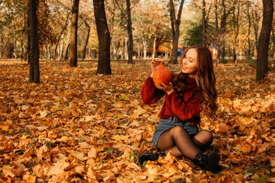 Young beautiful smiling woman with long curly hair holding orange halloween pumpkin on autumn park 