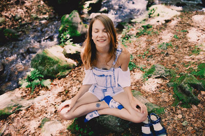 Beautiful young girl meditating doing yoga outdoors in summer forest near the stream