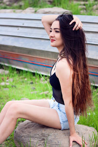 Side view of beautiful woman sitting on rock at field