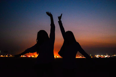Silhouette women standing by sea against sky at night
