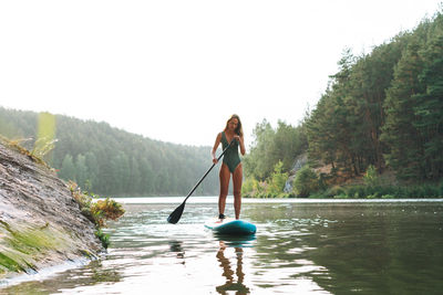 The young woman in green sweemsuit on sup boat with oar floating on river, weekend trip and travel