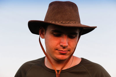 Young man smiling farmer in cowboy hat at field against blue sky. portrait of millennial man